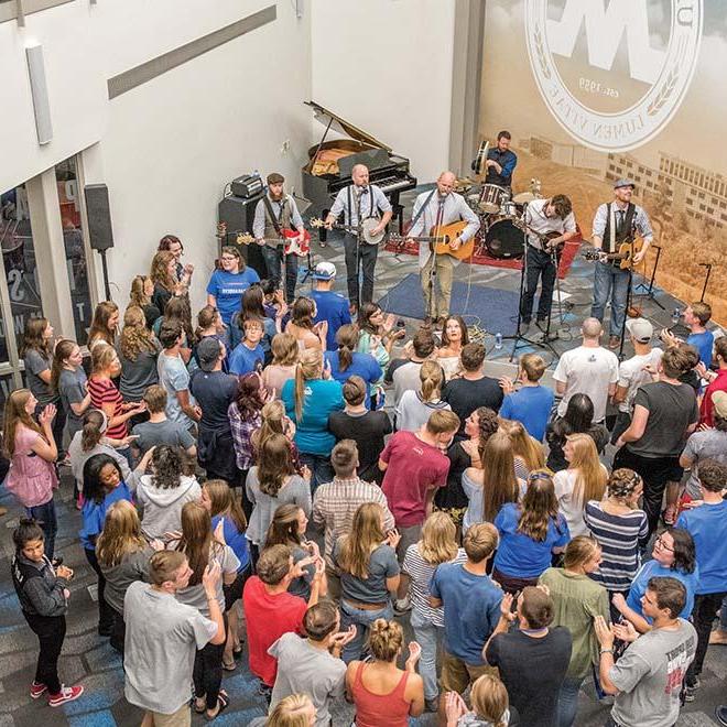 A band on stage playing for a large group of energetic students in the lower level of the university center